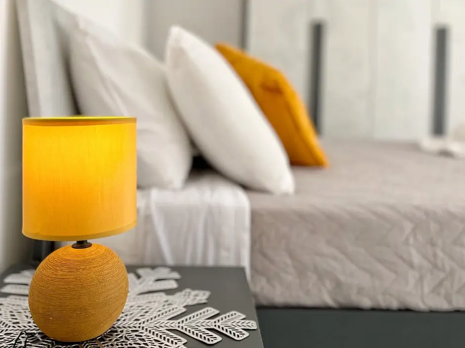 Comfortable bedroom with a yellow bedside lamp, decorative pillows, and a minimalist design, representing vacation rental management services in Malta