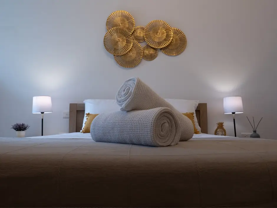 Modern bedroom with rolled towels, golden wall decor, and cozy lighting, representing vacation rental management services in Malta