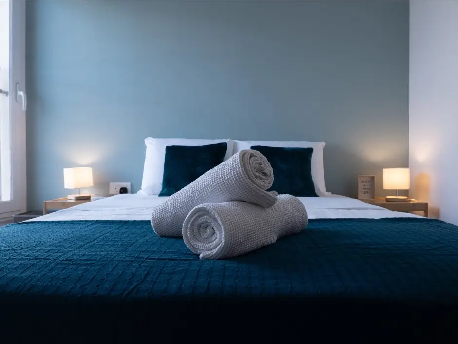 Stylish bedroom with blue bedding, rolled towels, and warm lighting, showcasing professional vacation rental management services in Malta