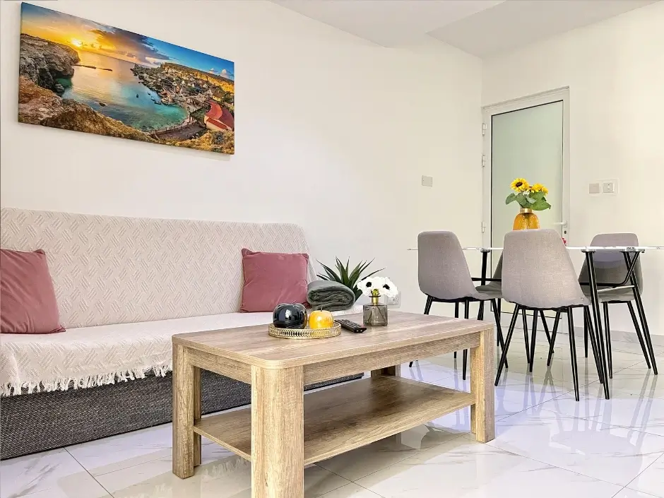 Bright living room with a wooden coffee table, sofa, and dining area featuring vibrant decor and natural lighting, highlighting short-term rental management services in Malta