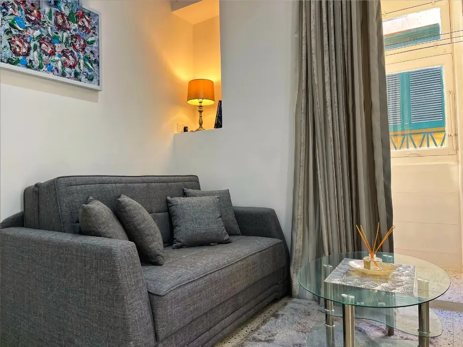 Stylish living room with a gray sofa, glass table, and artistic decor, highlighting short-term rental management services in Malta