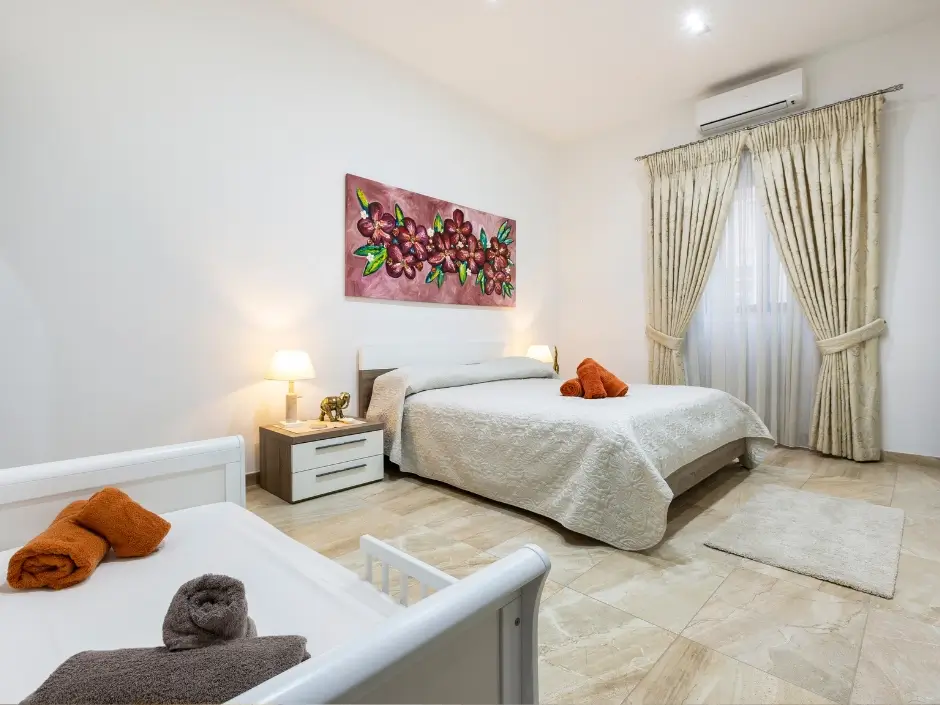 Bright bedroom with floral artwork, a double bed, and a single bed, showcasing professional property management services in Malta