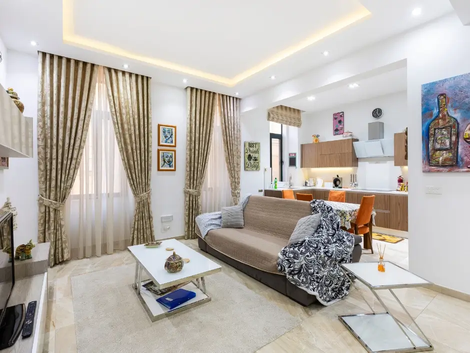 Elegant living room with curtains, sofa, and integrated kitchen area, highlighting short-term rental management services in Malta